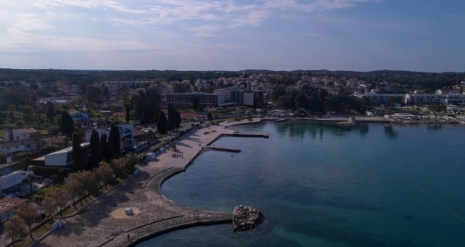 Die wunderschöne Küstenlinie von Poreč, Istrien – kristallklares Wasser, Palmenpromenade und historische Gebäude direkt am Meer.